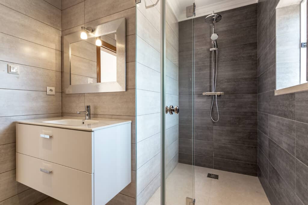 Salle de bain moderne carrelée gris clair et foncé avec lavabo, miroir éclairé, douche à l'italienne et robinetterie chromée.
